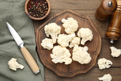 Photo of Fresh raw cauliflower florets, spices and knife on wooden table, flat lay