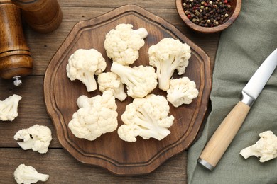 Photo of Fresh raw cauliflower florets, spices and knife on wooden table, flat lay