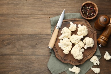 Photo of Fresh raw cauliflower florets, spices and knife on wooden table, flat lay. Space for text