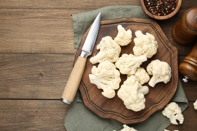 Photo of Fresh raw cauliflower florets, spices and knife on wooden table, flat lay. Space for text