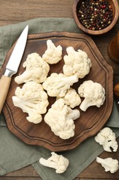 Photo of Fresh raw cauliflower florets, spices and knife on wooden table, flat lay