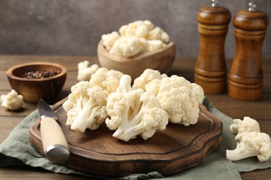 Photo of Fresh raw cauliflower florets, spices and knife on wooden table, closeup