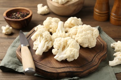 Photo of Fresh raw cauliflower florets, spices and knife on wooden table, closeup