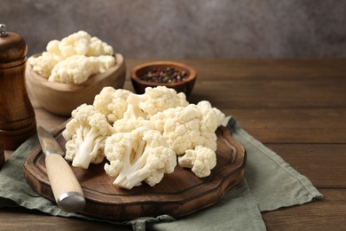 Photo of Fresh raw cauliflower florets, spices and knife on wooden table, closeup. Space for text