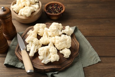 Photo of Fresh raw cauliflower florets, spices and knife on wooden table, closeup. Space for text