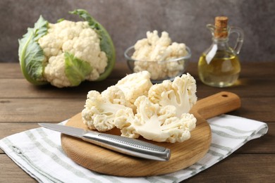 Photo of Fresh raw cauliflower florets, knife and oil on wooden table, closeup