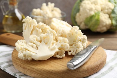 Photo of Fresh raw cauliflower florets, knife and oil on table, closeup