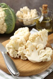 Photo of Fresh raw cauliflower florets, knife and oil on table, closeup