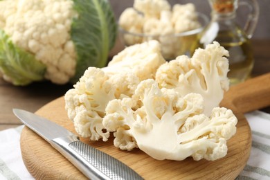 Photo of Fresh raw cauliflower florets, knife and oil on table, closeup