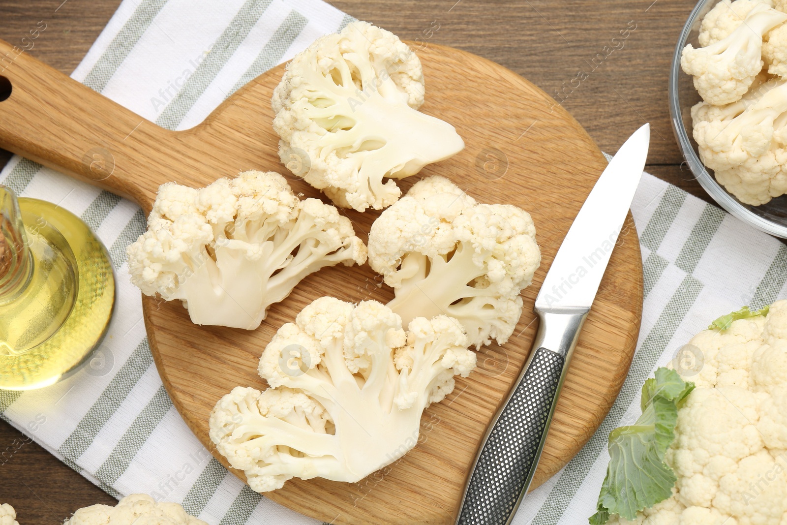 Fresh raw cauliflower florets, knife and oil on wooden table, flat lay Photo of Fresh raw cauliflower florets, knife and oil on wooden table, flat lay