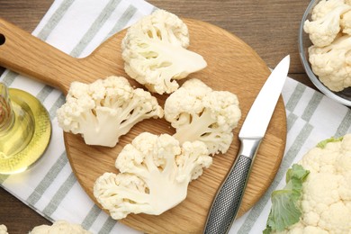 Photo of Fresh raw cauliflower florets, knife and oil on wooden table, flat lay