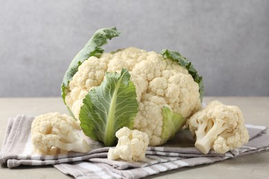 Photo of Fresh cauliflower with green leaves on light grey table, closeup