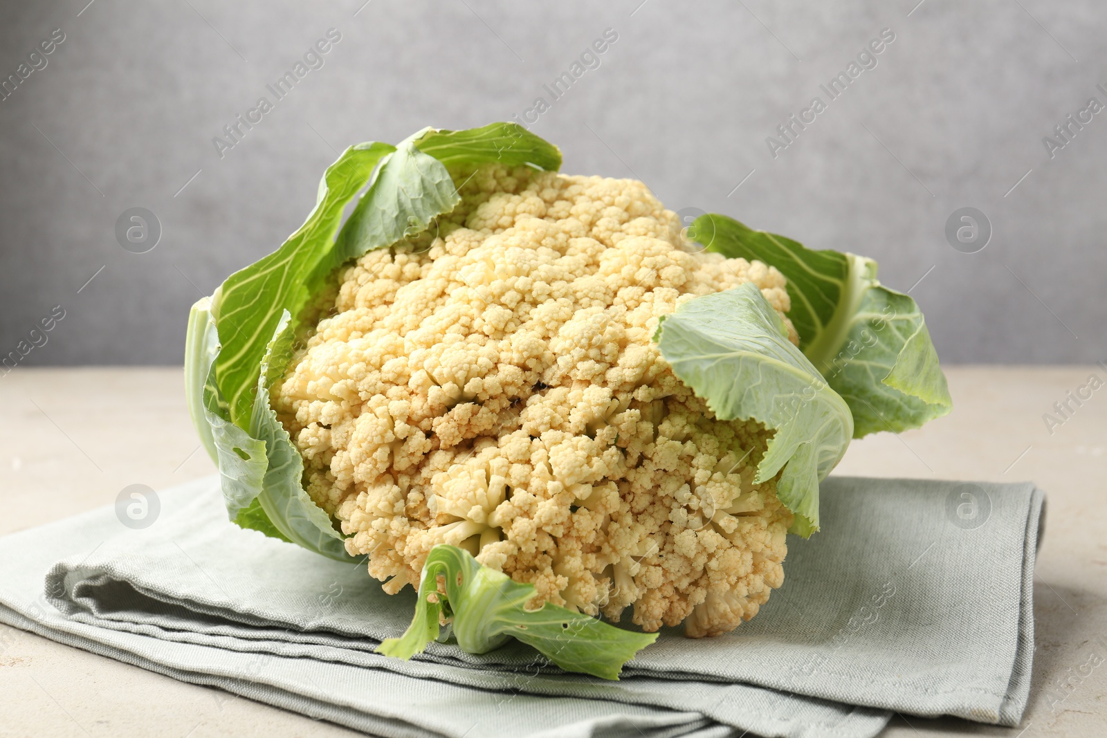 Photo of Fresh cauliflower with green leaves on light grey table, closeup
