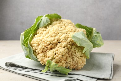 Photo of Fresh cauliflower with green leaves on light grey table, closeup