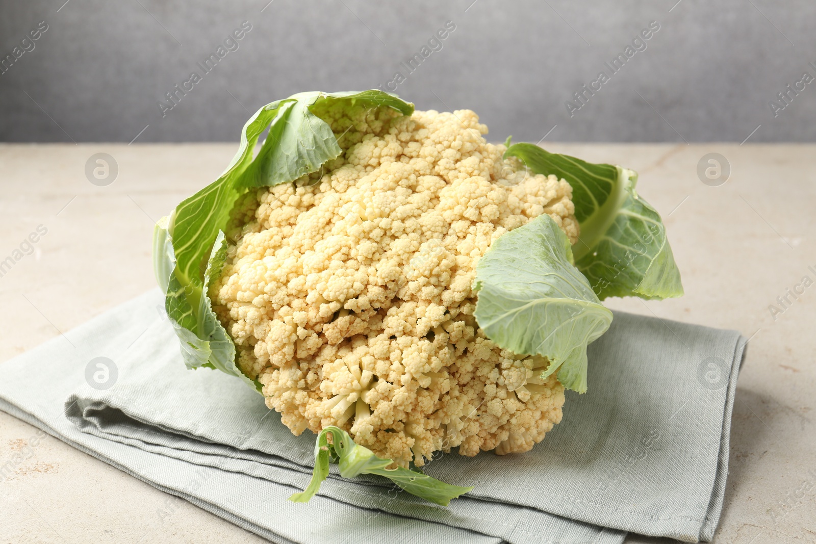Photo of Fresh cauliflower with green leaves on light grey table, closeup