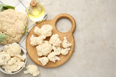 Photo of Fresh raw cauliflower florets and oil on light grey table, flat lay. Space for text