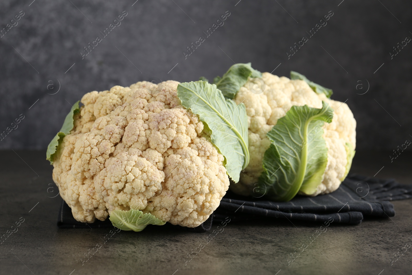 Photo of Fresh cauliflower heads with green leaves on grey table