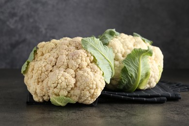 Photo of Fresh cauliflower heads with green leaves on grey table