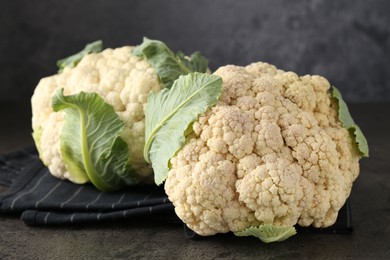 Photo of Fresh cauliflower heads with green leaves on grey table, closeup