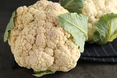 Photo of Fresh cauliflower heads with green leaves on grey table, closeup