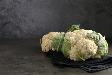 Photo of Fresh cauliflower heads with green leaves on grey table, closeup. Space for text