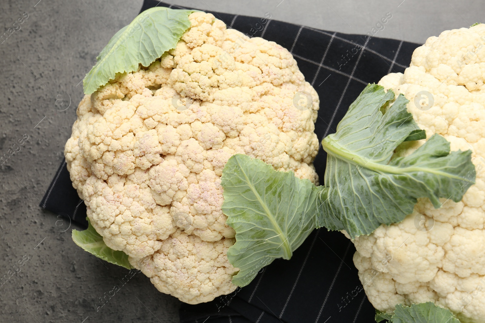 Photo of Fresh cauliflower heads with green leaves on grey table, flat lay