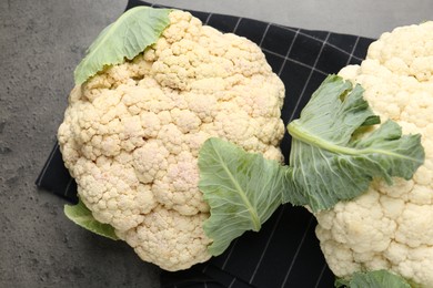Photo of Fresh cauliflower heads with green leaves on grey table, flat lay