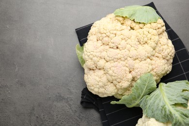 Photo of Fresh cauliflower head with green leaves on grey table, top view. Space for text