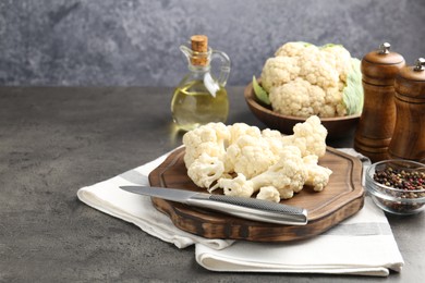 Photo of Fresh raw cauliflower florets, spices and knife on grey table, closeup. Space for text