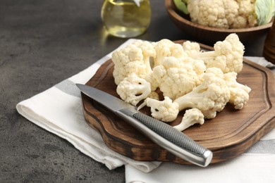 Photo of Fresh raw cauliflower florets, knife and oil on grey table, closeup. Space for text
