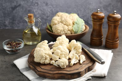 Photo of Fresh raw cauliflower florets, spices and knife on grey table, closeup