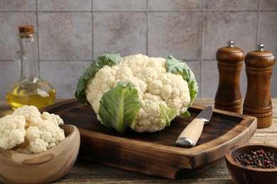 Photo of Fresh cauliflower with green leaves, spices and knife on wooden table, closeup