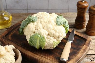 Photo of Fresh cauliflower with green leaves, spices and knife on wooden table, closeup