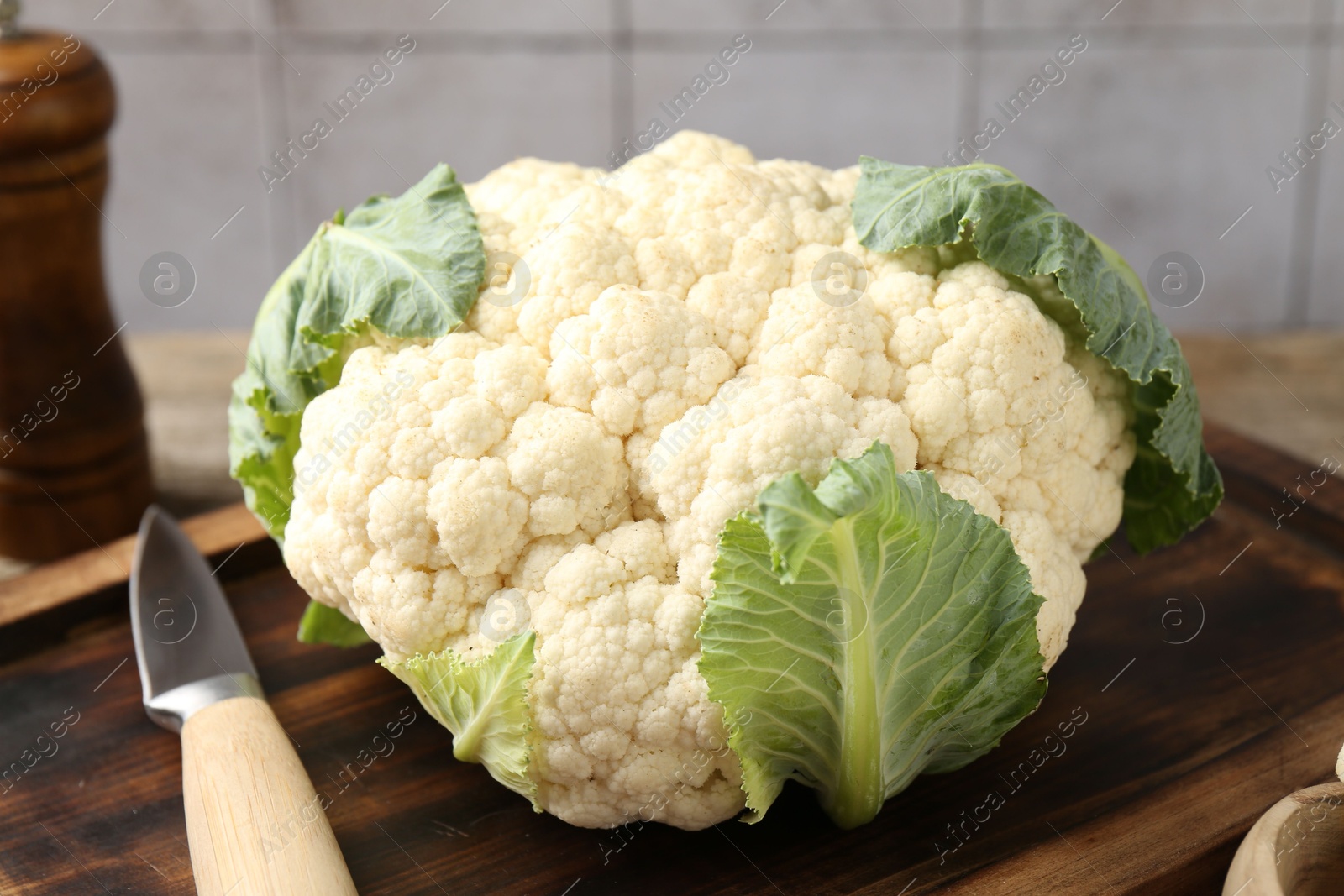 Fresh cauliflower with green leaves and knife on table, closeup Photo of Fresh cauliflower with green leaves and knife on table, closeup