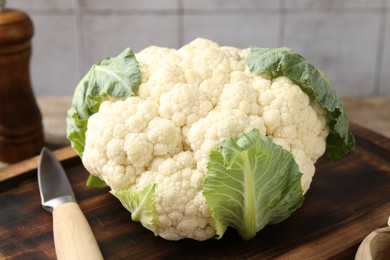 Photo of Fresh cauliflower with green leaves and knife on table, closeup