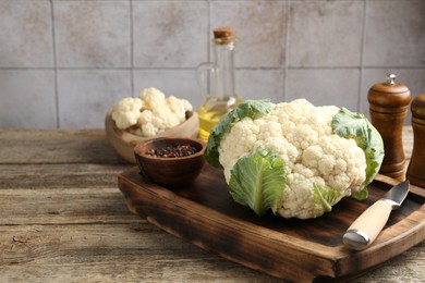 Photo of Fresh cauliflower with green leaves, spices and knife on wooden table, closeup. Space for text