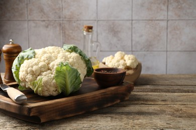 Photo of Fresh cauliflower with green leaves, spices and knife on wooden table, closeup. Space for text