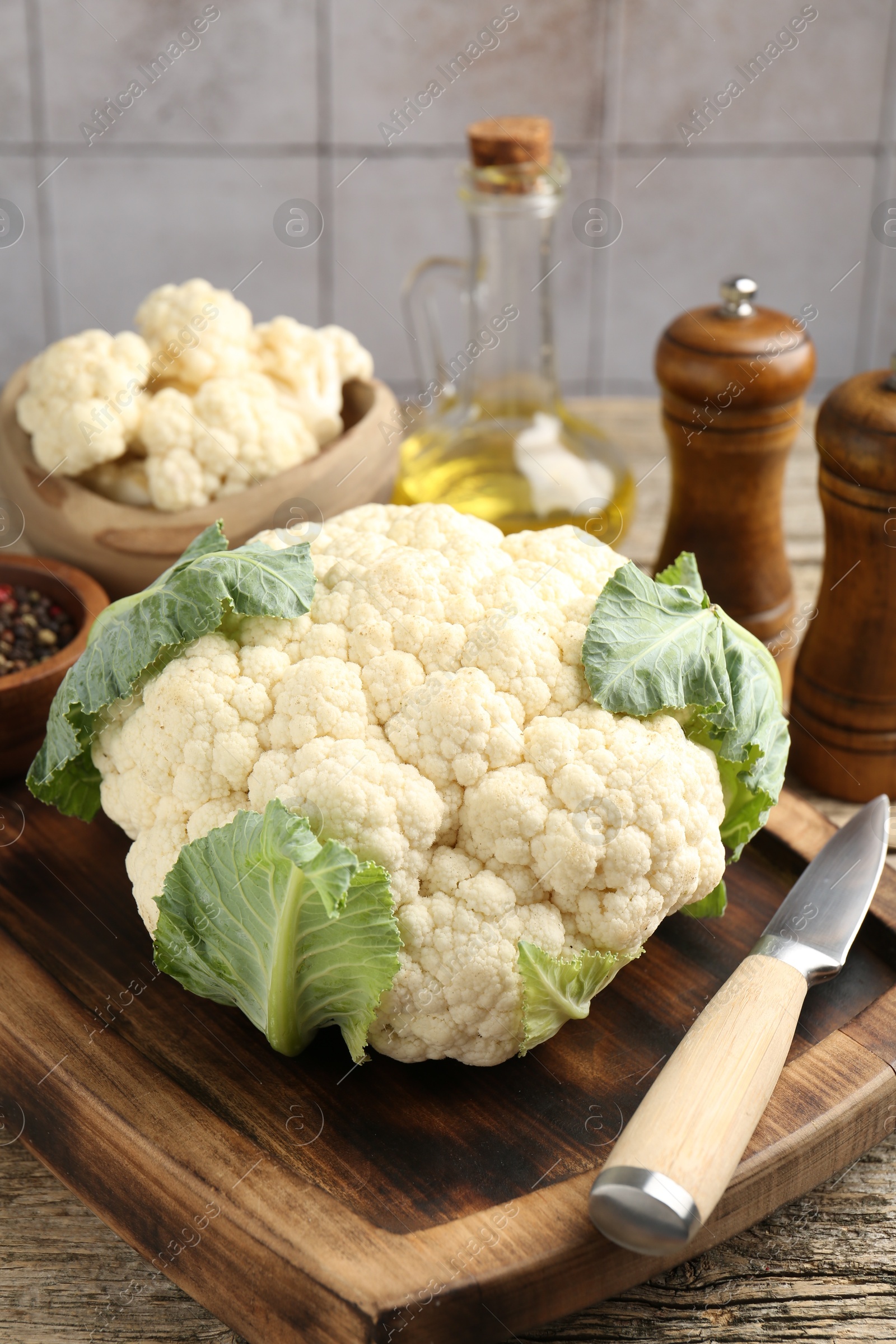 Fresh cauliflower with green leaves, spices and knife on wooden table, closeup Photo of Fresh cauliflower with green leaves, spices and knife on wooden table, closeup
