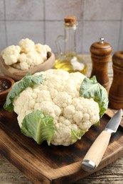 Photo of Fresh cauliflower with green leaves, spices and knife on wooden table, closeup