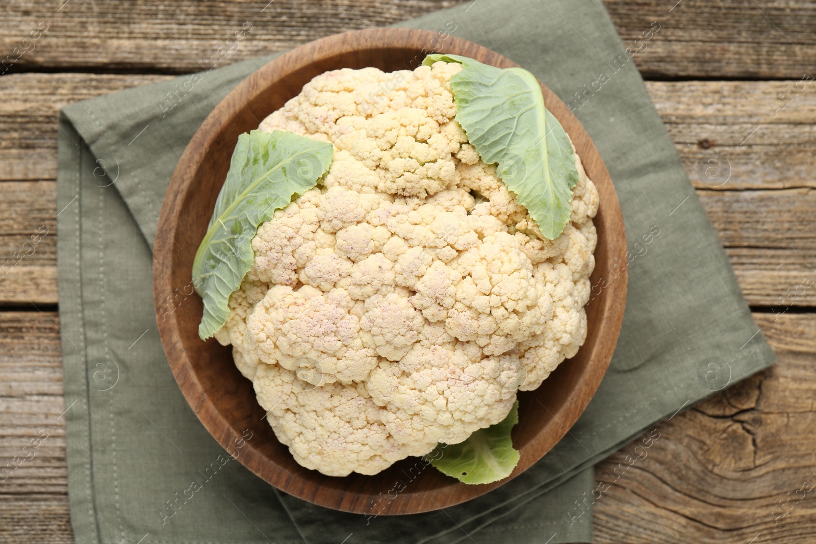 Photo of Fresh cauliflower with green leaves on wooden table, top view