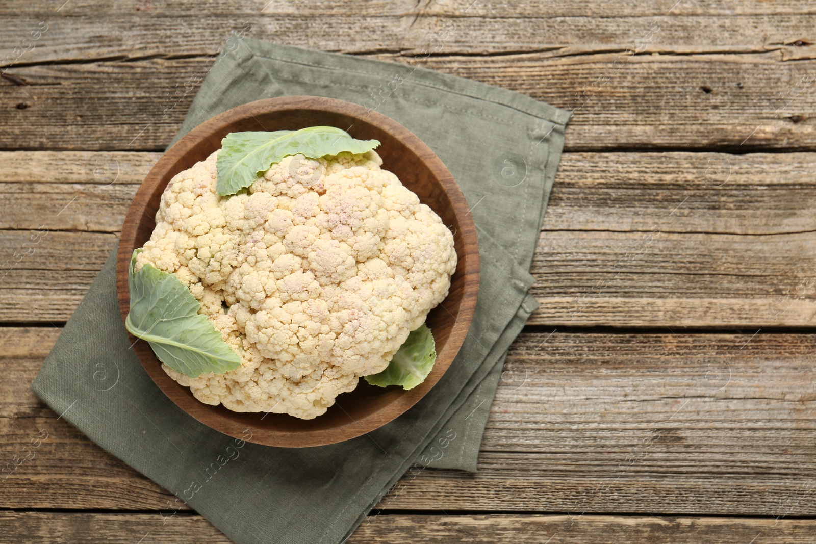 Photo of Fresh cauliflower with green leaves on wooden table, top view. Space for text