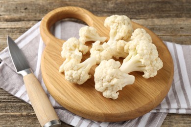 Photo of Fresh raw cauliflower florets and knife on wooden table, closeup