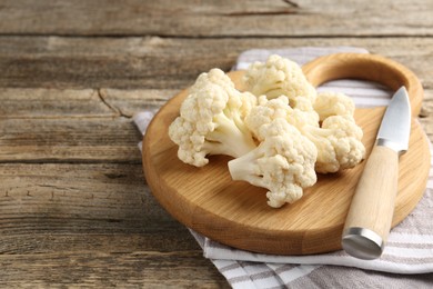 Photo of Fresh raw cauliflower florets and knife on wooden table, closeup. Space for text