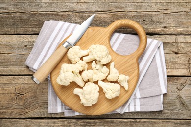 Photo of Fresh raw cauliflower florets and knife on wooden table, top view