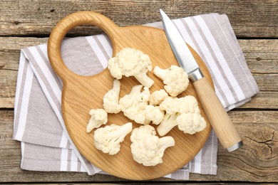 Photo of Fresh raw cauliflower florets and knife on wooden table, top view
