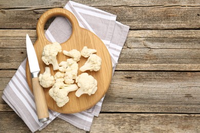 Photo of Fresh raw cauliflower florets and knife on wooden table, top view. Space for text