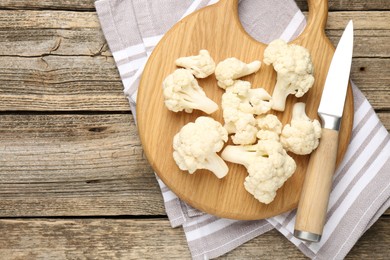 Photo of Fresh raw cauliflower florets and knife on wooden table, top view. Space for text