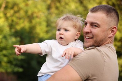 Photo of Smiling dad and his newborn baby looking at something outdoors. Happy Father's Day