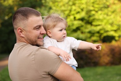 Photo of Smiling dad and his newborn baby looking at something outdoors. Happy Father's Day