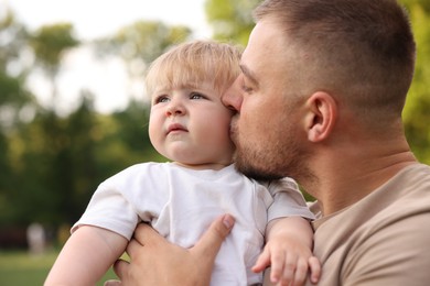 Photo of Dad kissing his cute newborn baby outdoors, closeup. Happy Father's Day